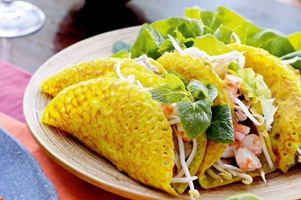 Những chiếc bánh xèo vàng gập đôi, lộ nhân tôm và giá, bày cùng rau.
